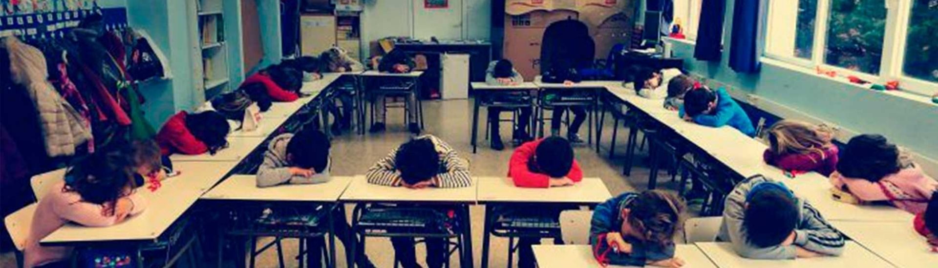 Foto de estudiantes apoyando su cabeza en las mesas de la sala de clases