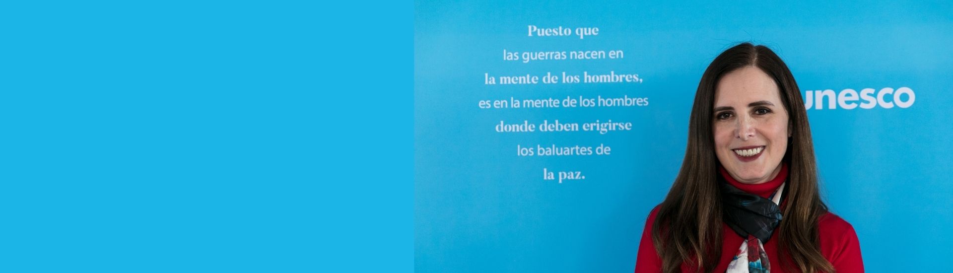 En la imagen se ve a la docente, Elisa Guerra, posando con un fondo azul que tiene una frase