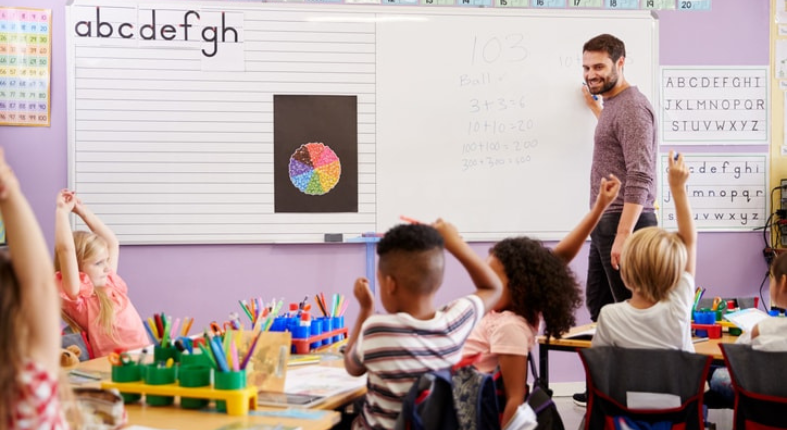 En la imagen se observa una sala de clases en la que un profesor realiza una actividad de matemáticas con estudiantes de alrededor de 5 a 6 años.